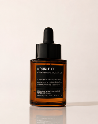 Nouri Bay Barrier Boosting Face Oil in an amber glass dropper bottle with a black dropper cap, set against a clean off-white background with a soft reflection, sensitive skin.